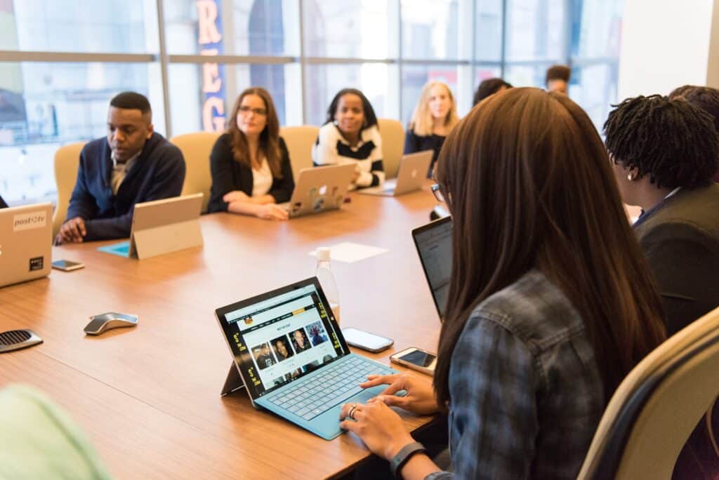 Reunião presencial com váriso colaboradores reunidos e a líder com dispositivo digital para passar imagens