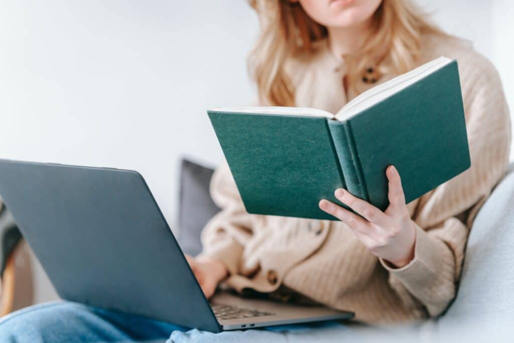 uma mulher com um notebook a sua esquerda e segura um livro com a mão esquerda, lê sobre a importância do SEO